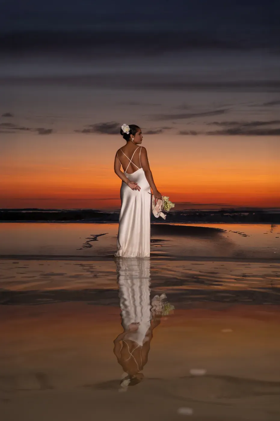 Noiva sozinha na lâmina de água, refletida contra o pôr do sol