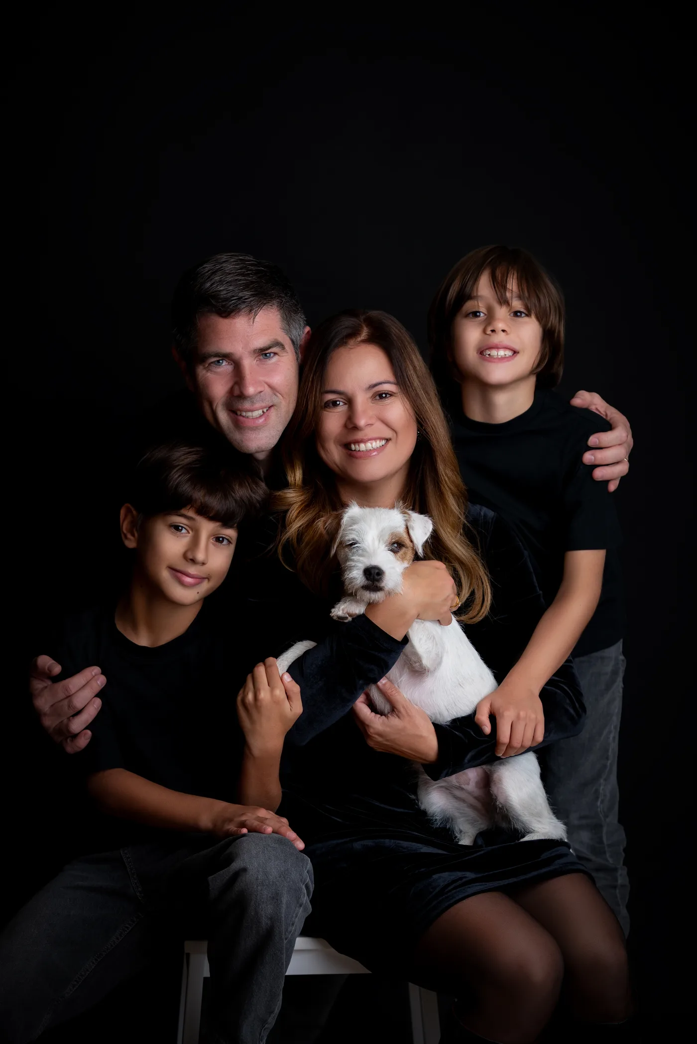 A mesma família em fundo preto, todos de preto, com o cachorro