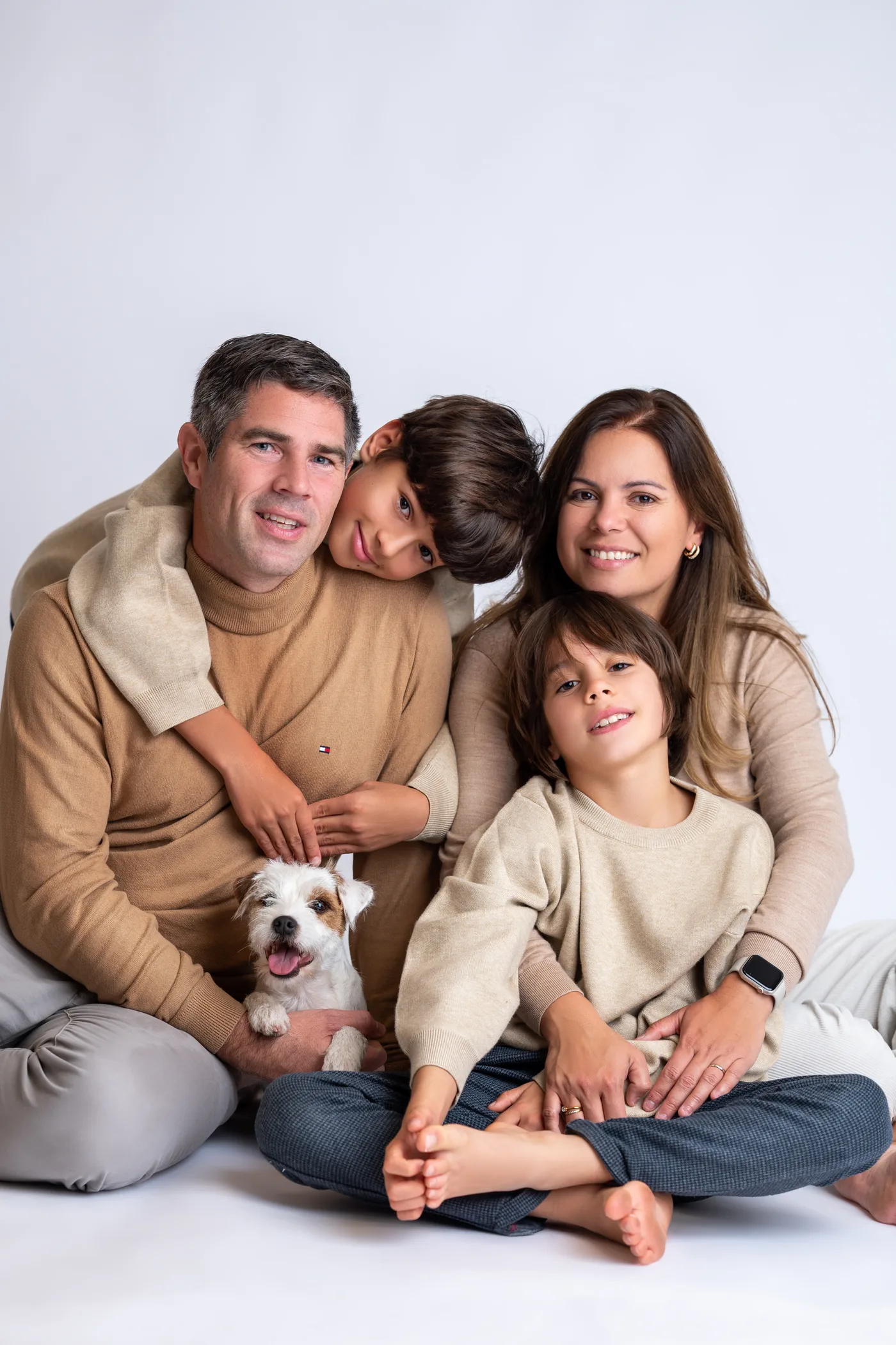 Família de quatro sentada em tons de bege, com o cachorro no colo