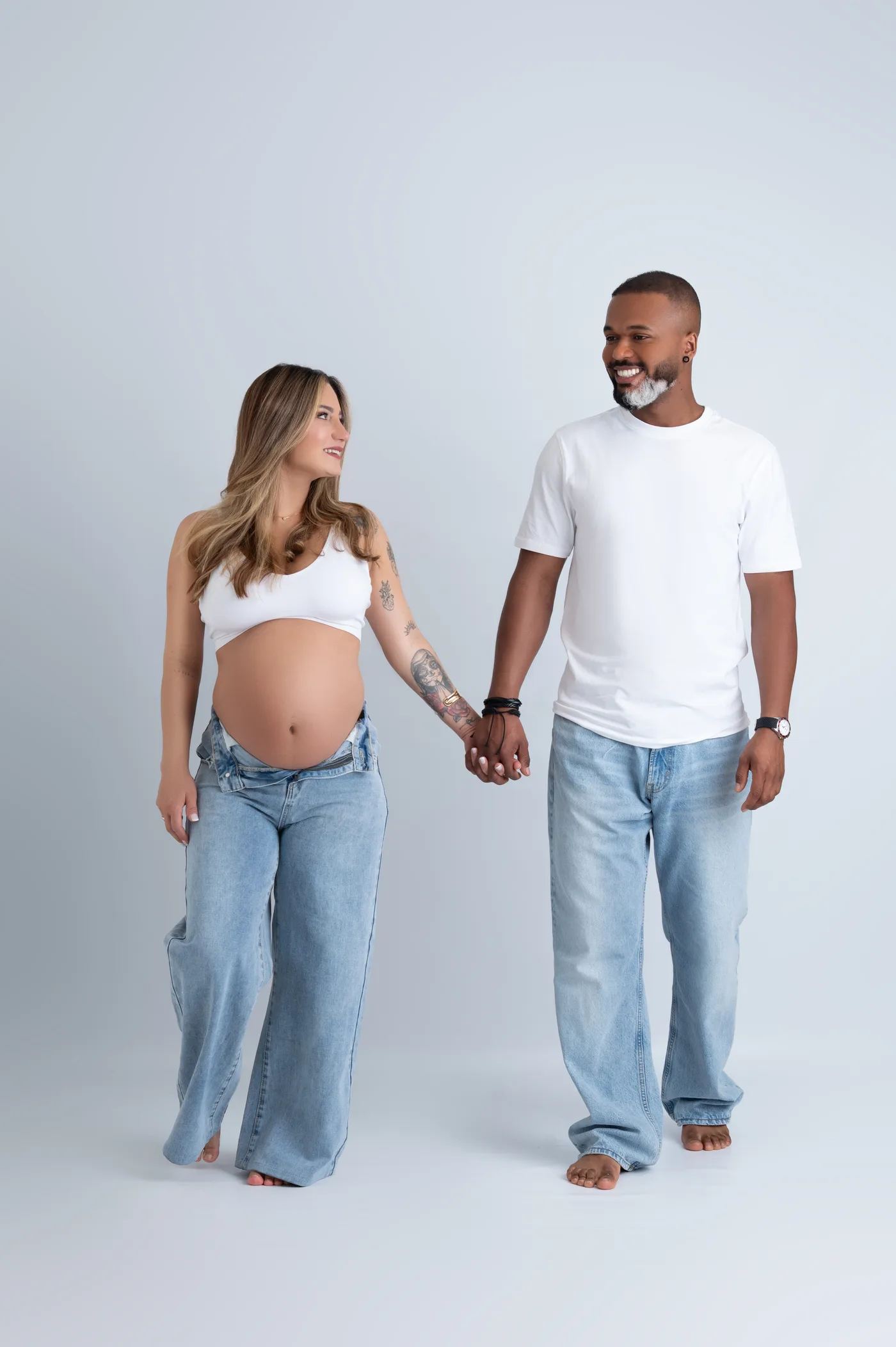 Casal grávido de mãos dadas, de pé, em fundo claro