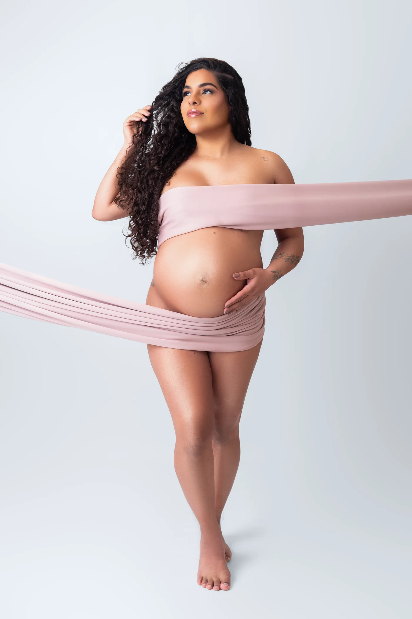 Gestante envolta num longo tecido rosa, mão na barriga
