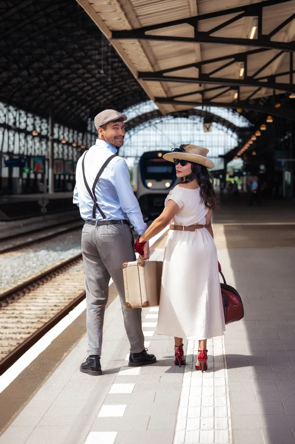 Casal de costas na plataforma da estação, malas na mão