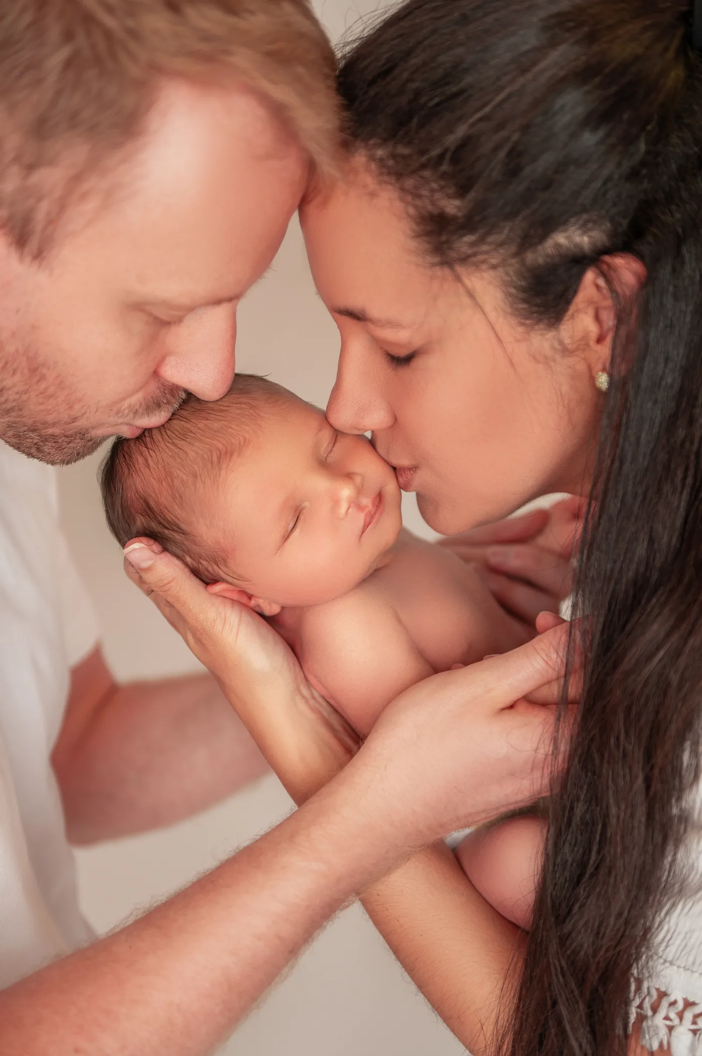 Pai e mãe beijando a cabeça do recém-nascido ao mesmo tempo