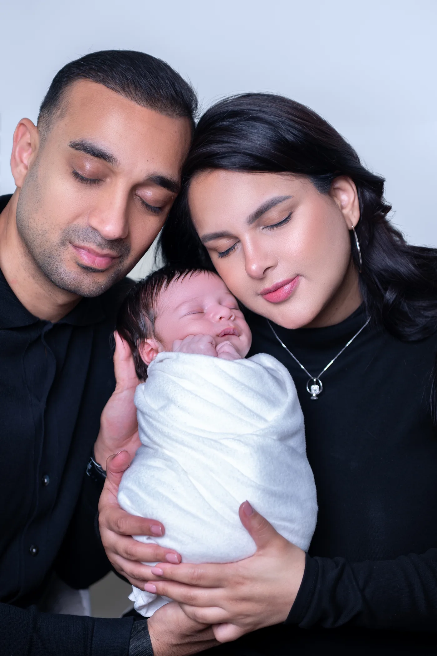 Casal com o recém-nascido enrolado, olhos fechados