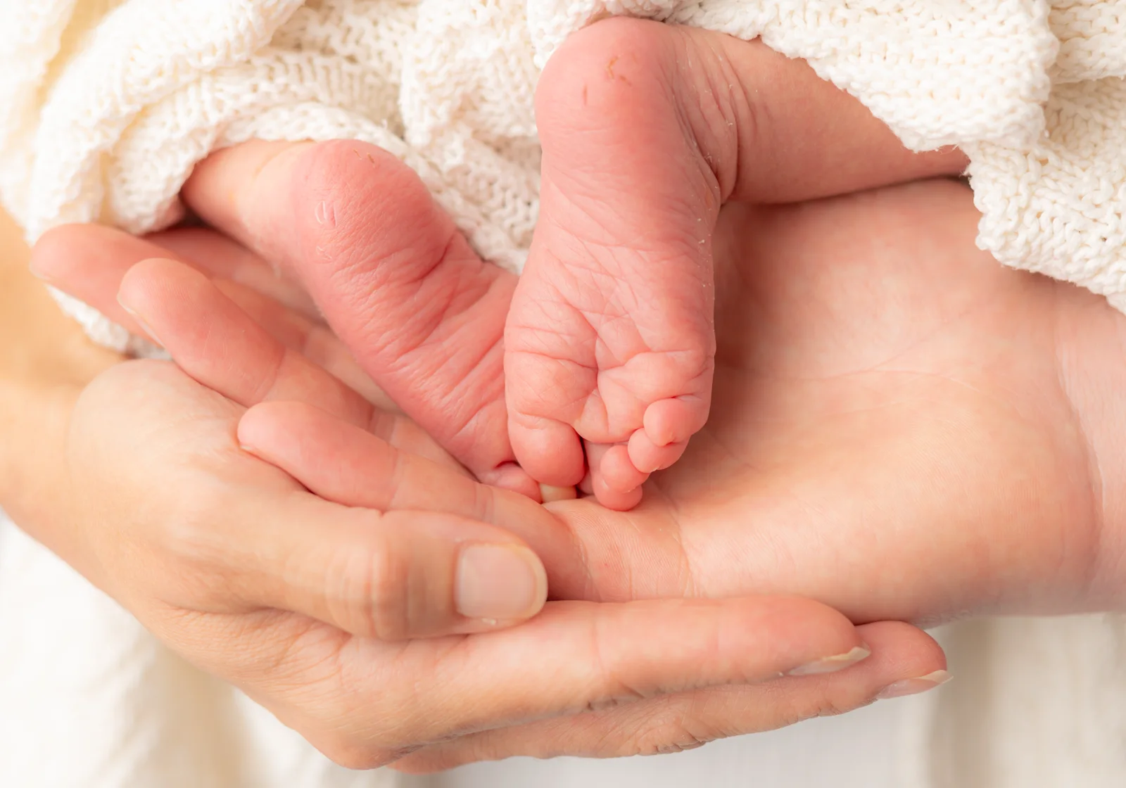 Os pés do recém-nascido apoiados nas mãos dos pais, em close