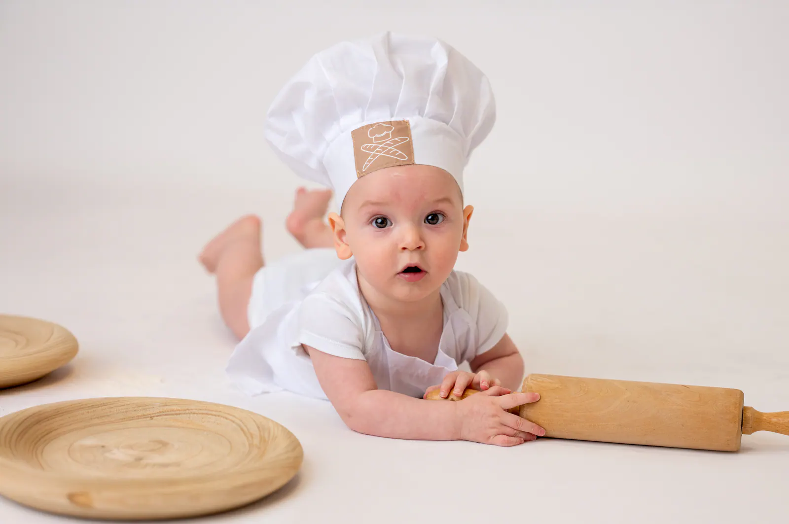 Bebê de touca de chef brincando com rolo de massa