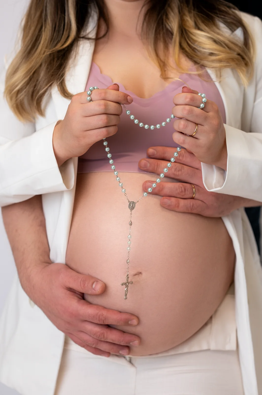 As mãos dela e as dele sobre a barriga, segurando um terço juntos