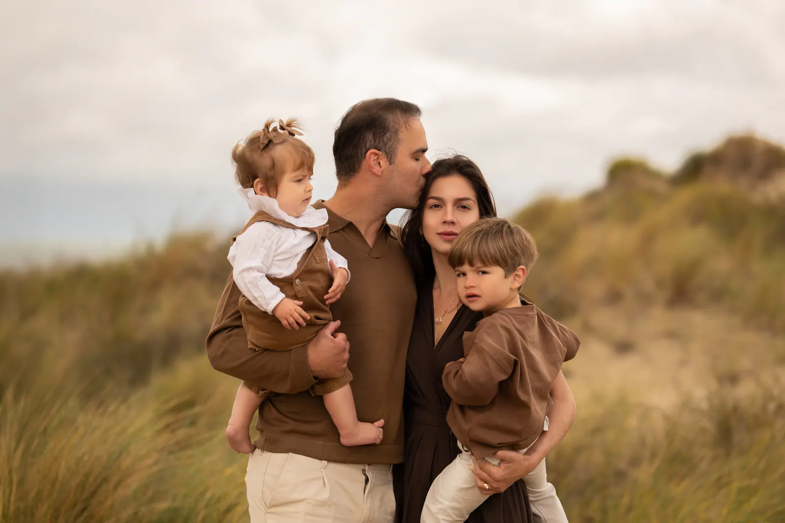 Pai e mãe com dois filhos pequenos nas dunas ao entardecer