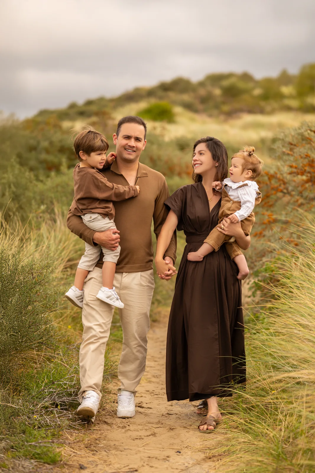 Casal com a filha pequena caminhando entre a vegetação alta das dunas